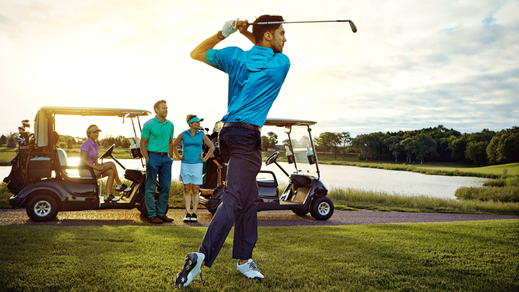 Golfer taking a swing with friends observing from golf carts
